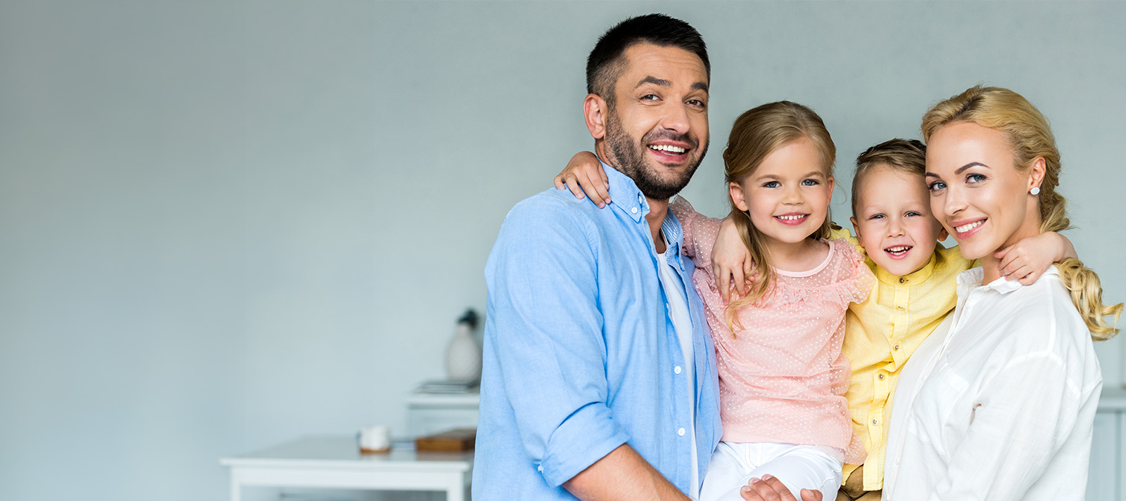 A family of four poses for a portrait with a warm and happy expression, in front of a modern kitchen setting.