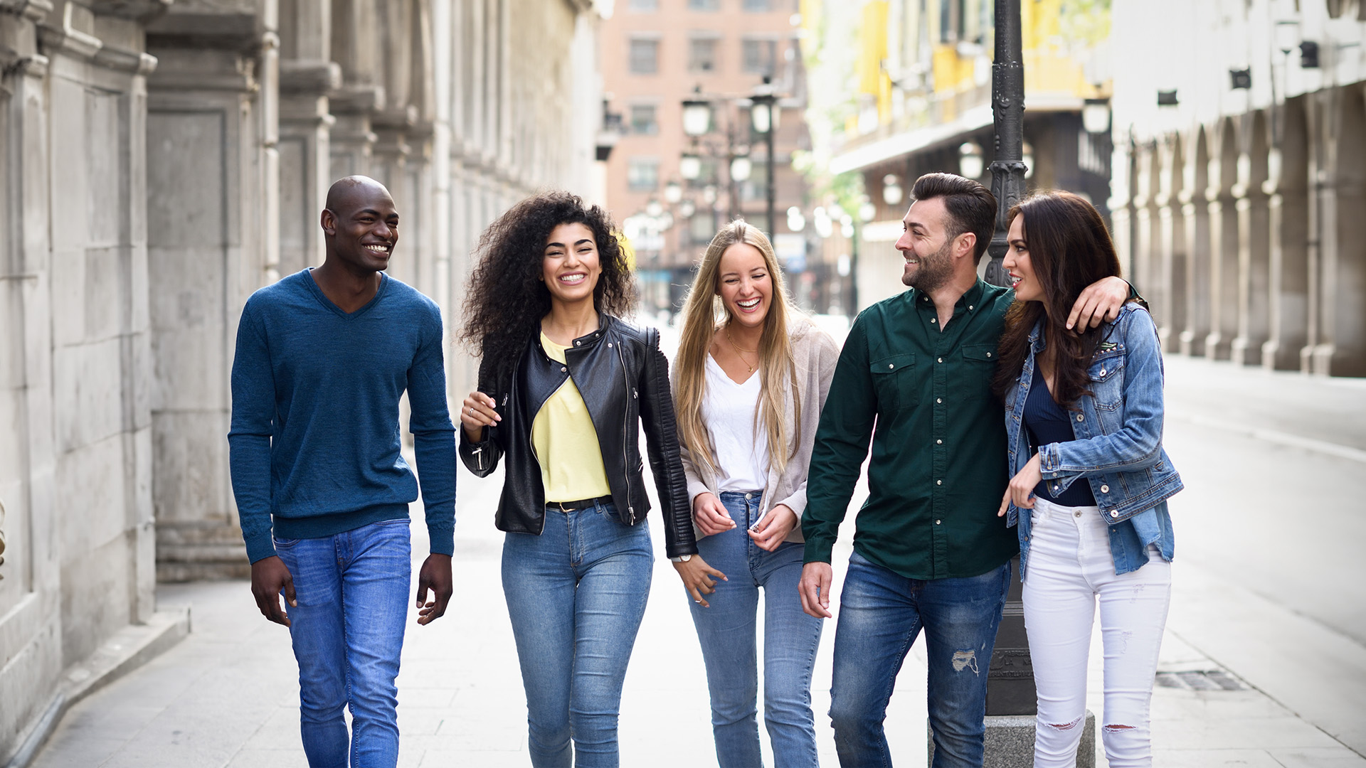 A group of friends poses for a photo on a city street, with one person holding a handbag.